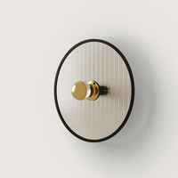 Schöne Wandleuchte 'Lass' von Aromas del Campo. Runder goldfarbener Teller aus Glas mit schwarz gefasstem Rand.