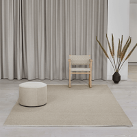 Teppich 'Escape Kelim' von Massimo aus Wolle in Hellbeige, natürlicher Stil, Lifestyle-Aufnahme in hellem Wohnzimmer mit Holzstuhl, rundem Pouf und Trockenblumen-Dekoration vor langen Leinenvorhängen