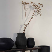 Vase 'Hero' von Tell Me More in Schwarz – Gruppe schwarzer Keramikvasen mit getrockneten Blütenzweigen auf rustikaler Holzbank, dunkles Wohndekor im minimalistischen Naturstil