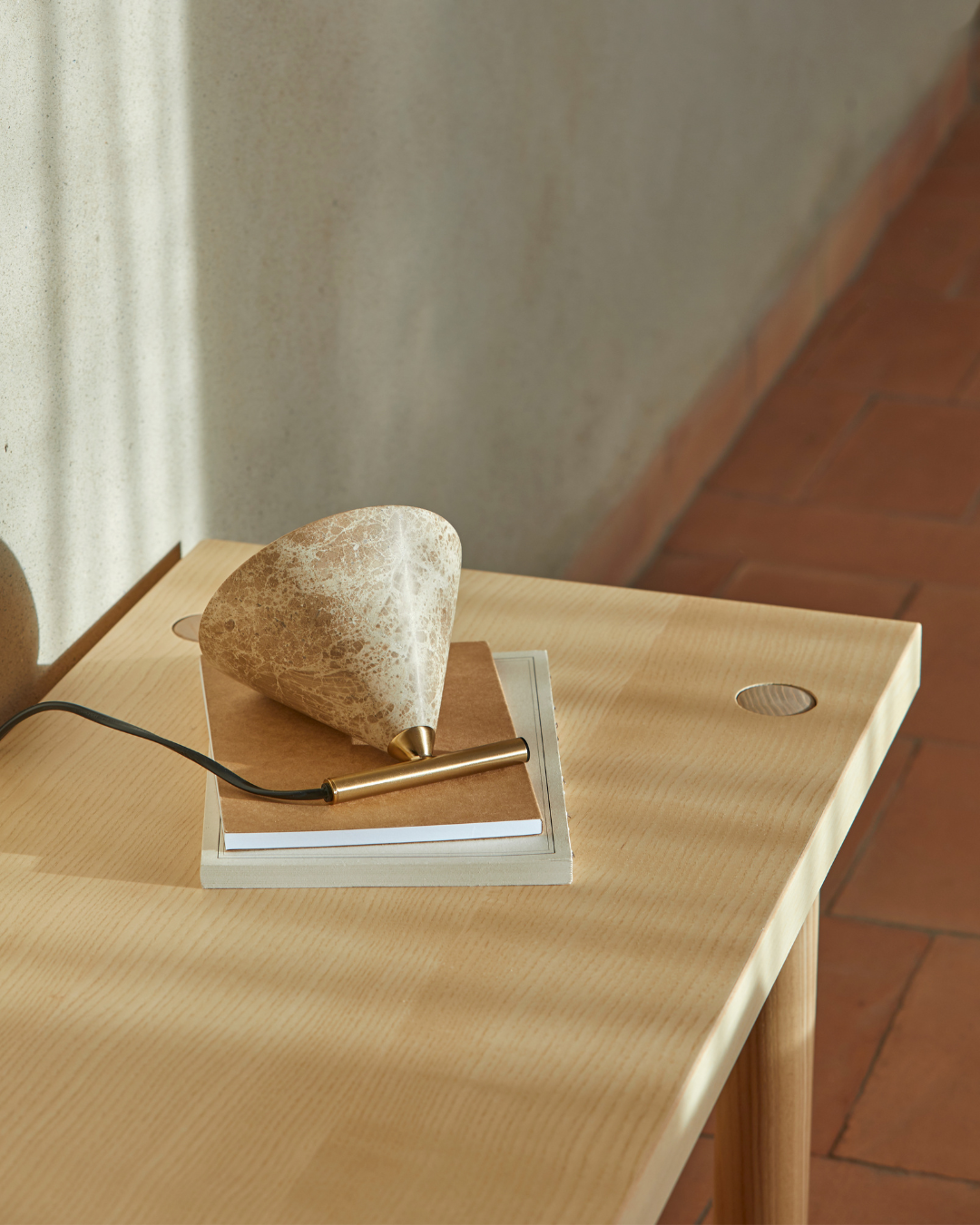 Nahaufnahme der Tischleuchte Iconic von Aromas del Campo, Marmor-Schirm mit goldenem Messing-Sockel auf einem Holztisch mit Terrakottaboden
