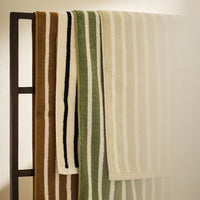 Badehandtuch 'Bonnie' von Tell Me More, 70x140 cm, aus 100% Bio-Baumwolle – alle Farbvarianten in Beige, Grün und Braun hängend an dunklem Handtuchhalter, minimalistisches Produktfoto
