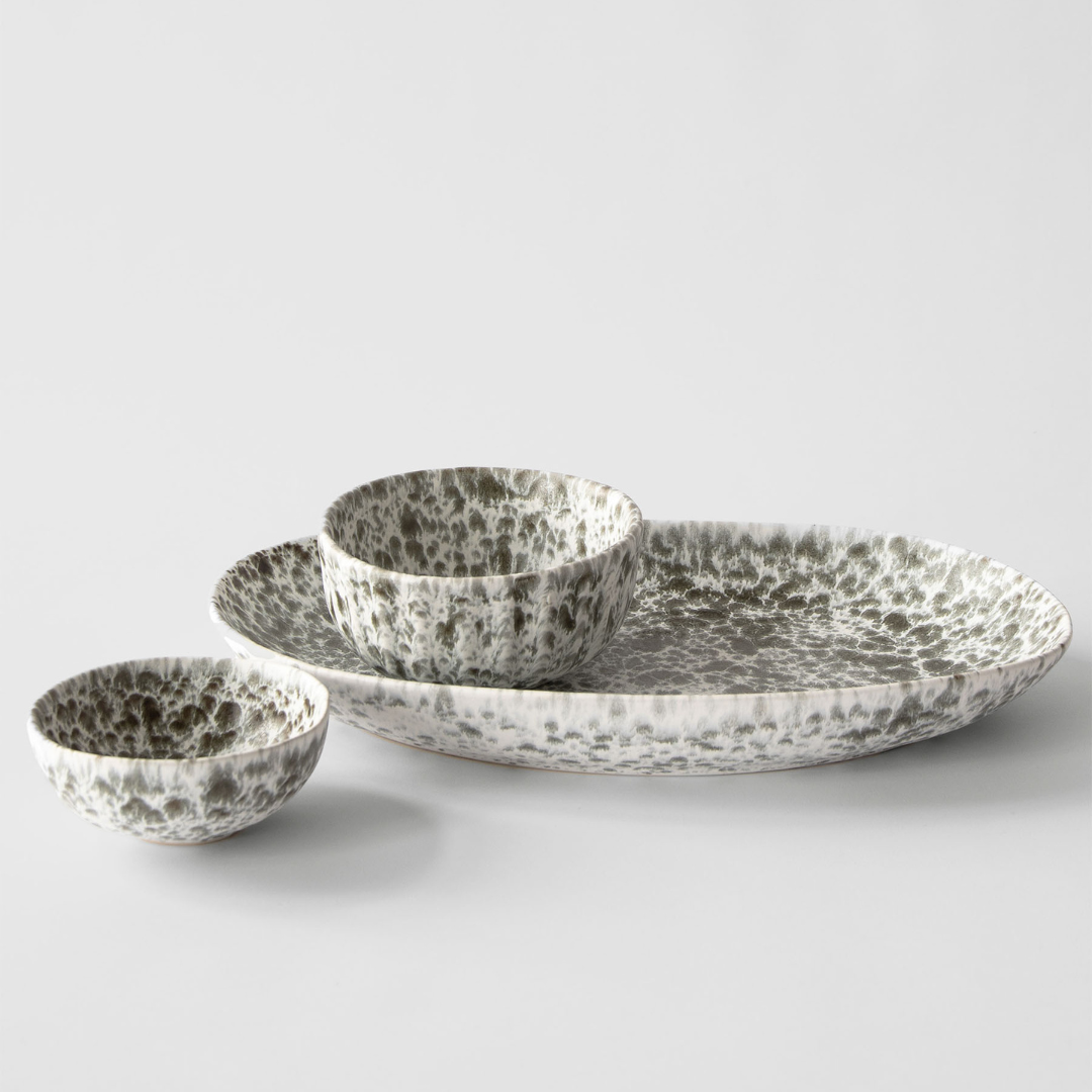 Keramikgeschirr-Set mit zwei Schalen und einer ovalen Platte in grün-weißer Sprenkelglasur, modernes handgefertigtes Design auf weißem Hintergrund.