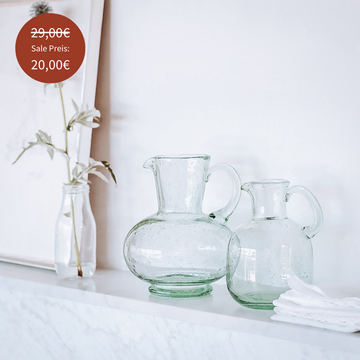 Handgefertigte Glaskaraffe der Marke Tell Me More aus recyceltem Glas, Modell ‘Garonne’, in zeitlosem skandinavischem Design auf weißem Marmorsims – dekorativ arrangiert mit Stoffservietten und einer Glasvase mit Trockenblume. Jetzt im Sale: Reduzierter Preis von 29,00€ auf 20,00€