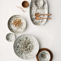 aServierschale ‘Rivoli’ von Tell Me More – Flatlay der Kollektion in verschiedenen Größen, weißes Porzellan mit olivgrünem Sprenkelmuster, Holzlöffel und Holzschälchen als Deko auf weißem Hintergrund