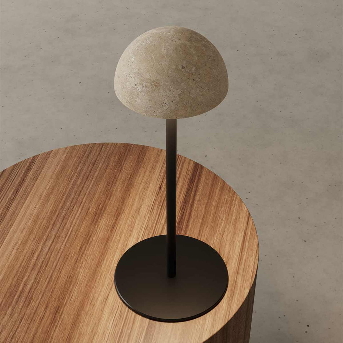 Tischleuchte Dussa von Aromas del Campo mit hellem Travertin‑Schirm und matt schwarzem Metallfuß.