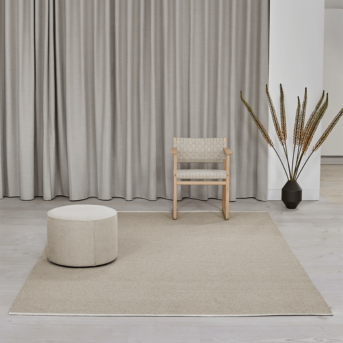 Teppich 'Escape Kelim' von Massimo aus Wolle in Hellbeige, natürlicher Stil, Lifestyle-Aufnahme in hellem Wohnzimmer mit Holzstuhl, rundem Pouf und Trockenblumen-Dekoration vor langen Leinenvorhängen