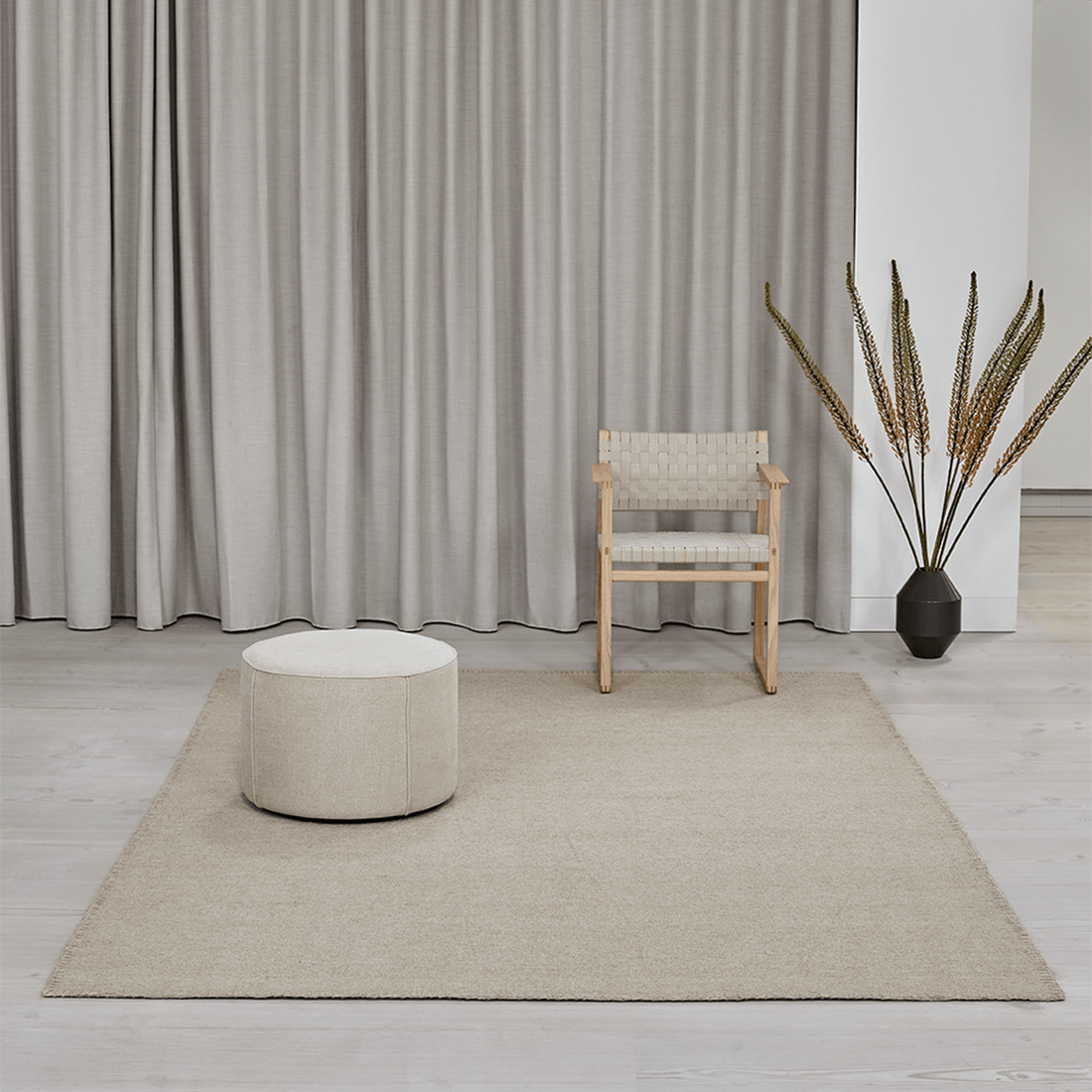 Teppich 'Escape Kelim' von Massimo aus Wolle in Hellbeige, natürlicher Stil, Lifestyle-Aufnahme in hellem Wohnzimmer mit Holzstuhl, rundem Pouf und Trockenblumen-Dekoration vor Leinenvorhängen, Nähte auf der Teppichoberfläche sichtbar
