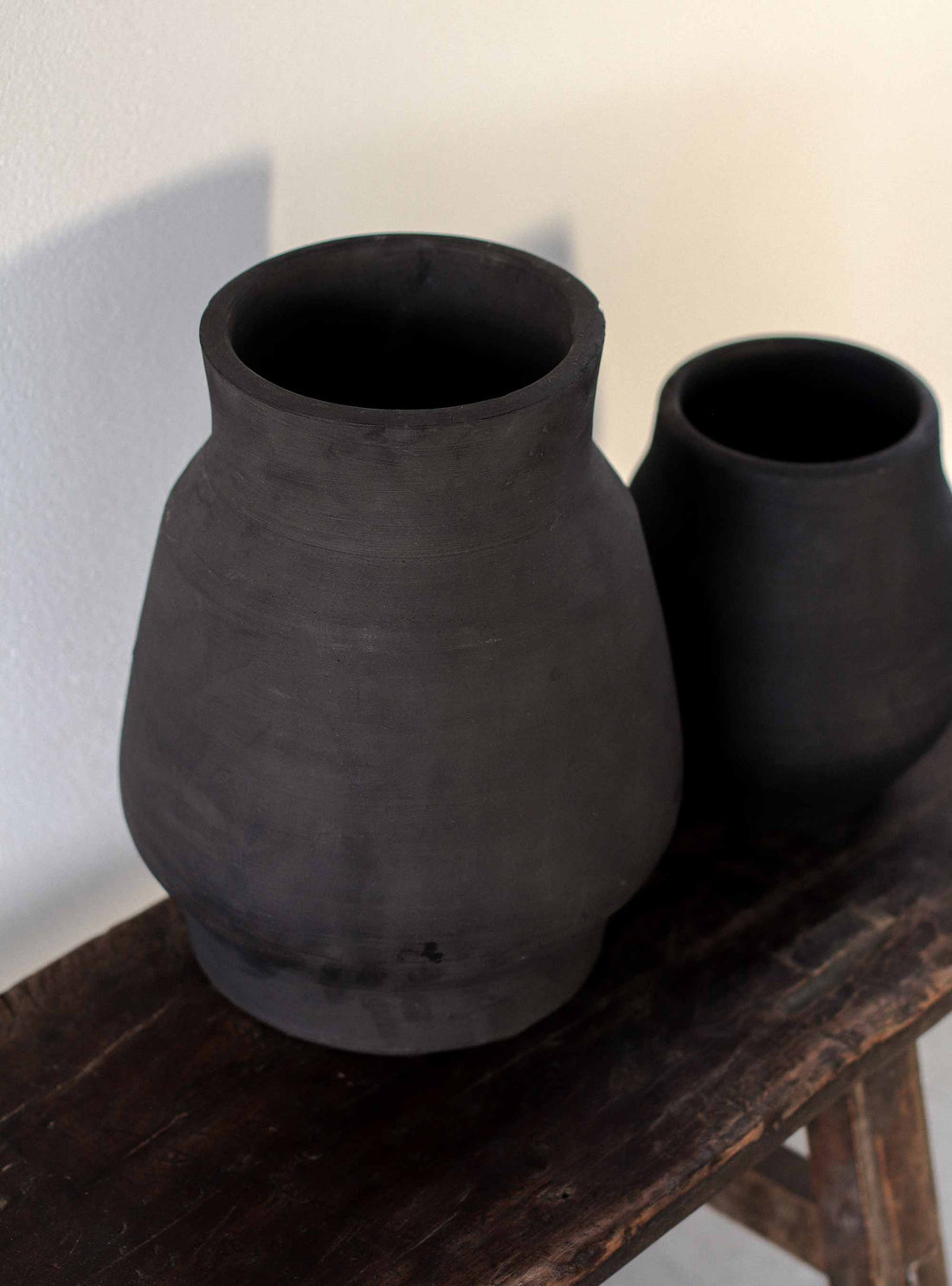 Vase 'Hero' groß und klein von Tell Me More im Größenvergleich – zwei schwarze Keramikvasen mit matter, rauer Oberfläche nebeneinander auf rustikalem Holztisch, Detailaufnahme der Handarbeit