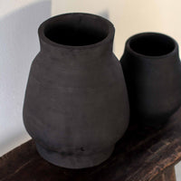 Vase 'Hero' groß und klein von Tell Me More im Größenvergleich – zwei schwarze Keramikvasen mit matter, rauer Oberfläche nebeneinander auf rustikalem Holztisch, Detailaufnahme der Handarbeit